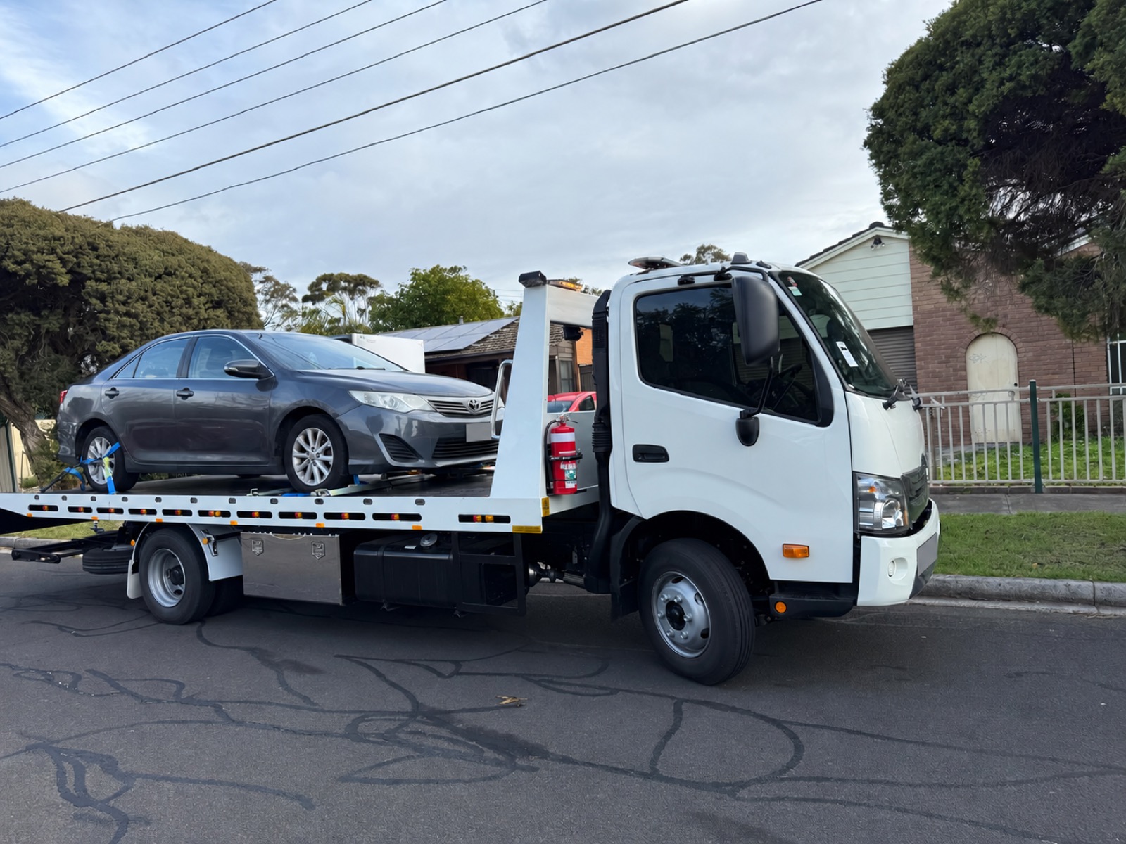 Grey sedan on a flatbed tow truck; registration details obscured.
