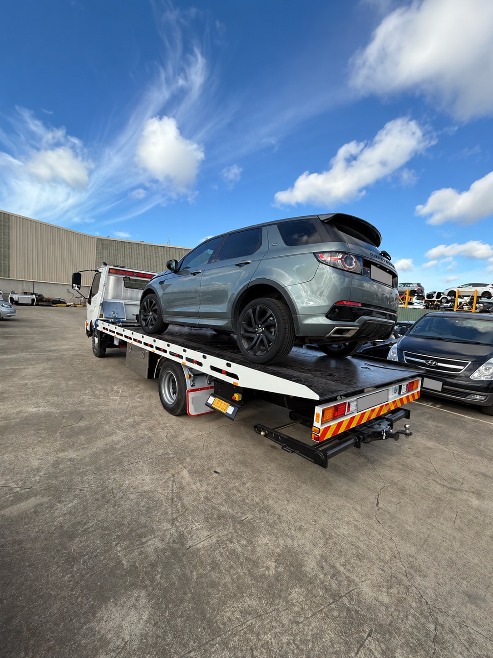 Grey SUV loaded on a flatbed tow truck; registration details obscured.